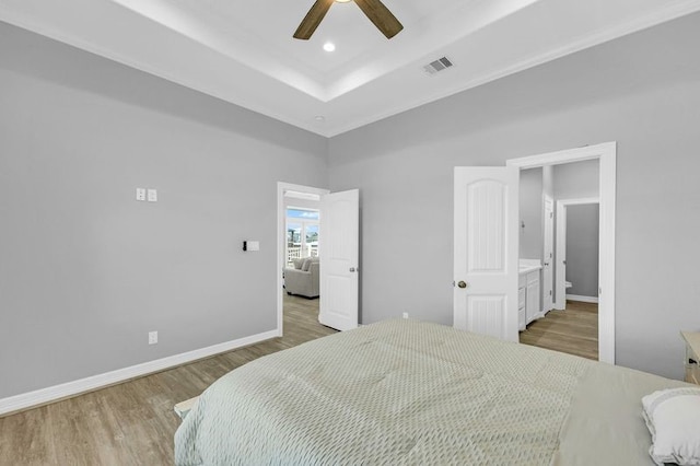 bedroom with wood-type flooring, a tray ceiling, ensuite bath, and ceiling fan