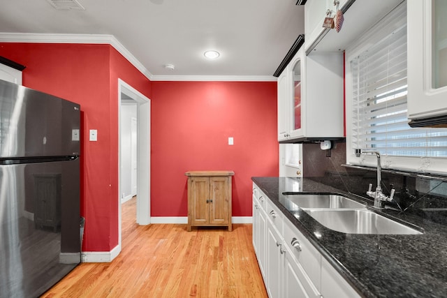 kitchen featuring white cabinets, sink, ornamental molding, light hardwood / wood-style floors, and stainless steel refrigerator