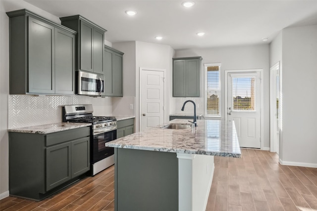 kitchen featuring sink, an island with sink, gray cabinets, appliances with stainless steel finishes, and hardwood / wood-style flooring