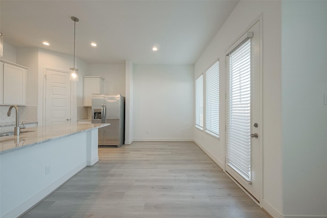 kitchen featuring light stone countertops, hanging light fixtures, stainless steel refrigerator with ice dispenser, decorative backsplash, and white cabinets