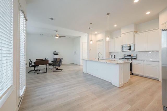 kitchen featuring an island with sink, light hardwood / wood-style floors, decorative light fixtures, white cabinets, and appliances with stainless steel finishes