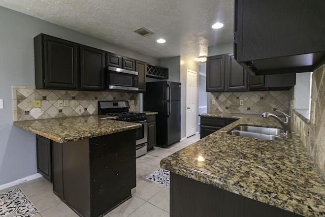 kitchen with sink, dark stone countertops, a textured ceiling, tasteful backsplash, and stainless steel appliances