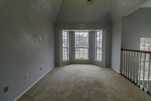 carpeted spare room featuring a textured ceiling, a wealth of natural light, and lofted ceiling