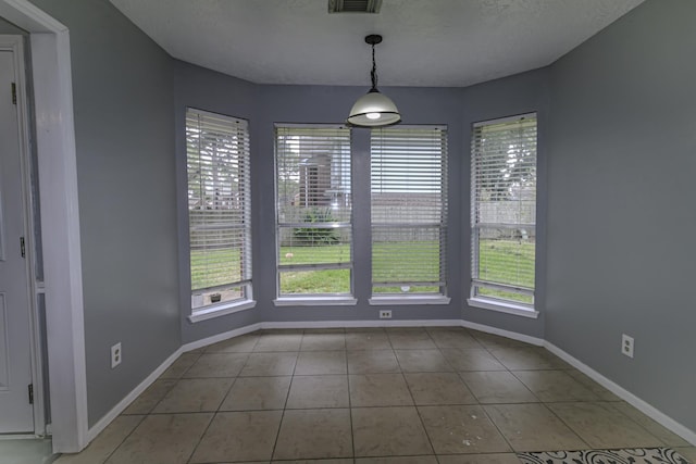 unfurnished dining area featuring a textured ceiling and light tile patterned flooring