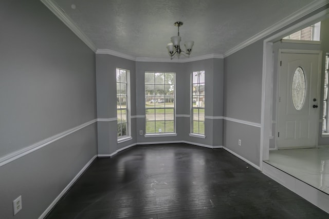 unfurnished dining area featuring a textured ceiling, dark wood-type flooring, crown molding, and an inviting chandelier