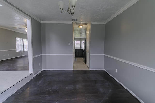 unfurnished dining area featuring ceiling fan with notable chandelier, ornamental molding, a textured ceiling, and dark wood-type flooring