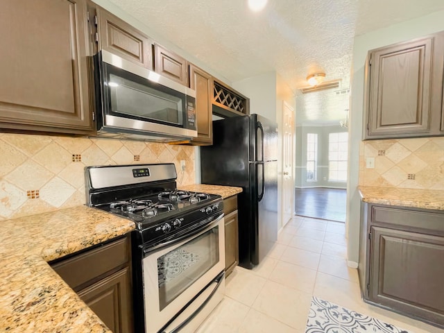 kitchen featuring light tile patterned floors, tasteful backsplash, appliances with stainless steel finishes, a textured ceiling, and baseboards