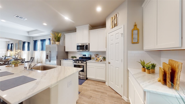 kitchen featuring light stone countertops, white cabinetry, sink, stainless steel appliances, and light hardwood / wood-style flooring