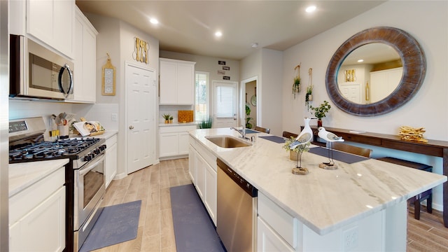 kitchen with white cabinetry, sink, light stone countertops, stainless steel appliances, and a kitchen island with sink