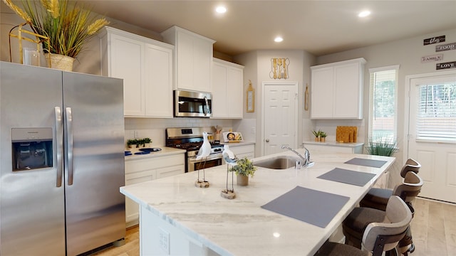 kitchen with a kitchen island with sink, sink, light stone countertops, and appliances with stainless steel finishes