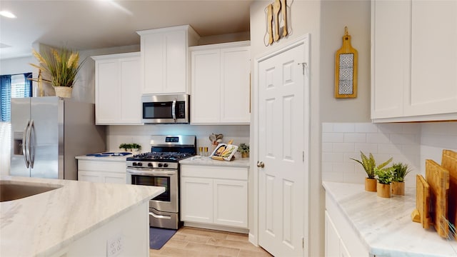 kitchen with light stone countertops, decorative backsplash, white cabinetry, and stainless steel appliances