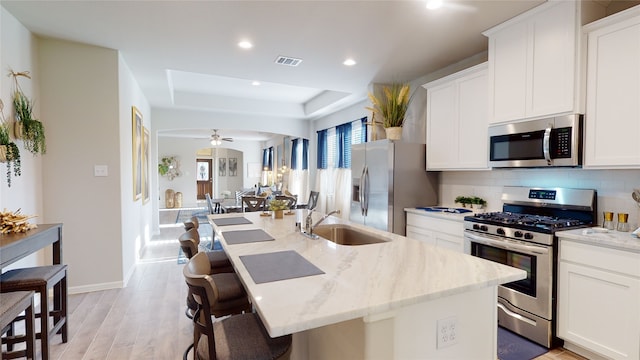 kitchen with stainless steel appliances, light stone counters, a center island with sink, and sink