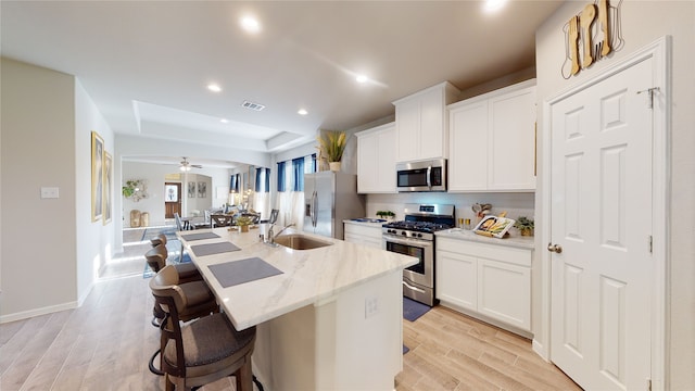 kitchen featuring a kitchen breakfast bar, stainless steel appliances, ceiling fan, white cabinets, and an island with sink