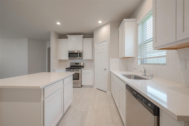 kitchen with light stone countertops, a center island, sink, stainless steel appliances, and white cabinets