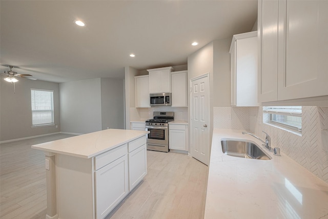 kitchen with light stone counters, stainless steel appliances, sink, white cabinets, and a center island