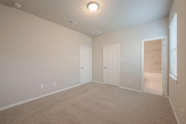 unfurnished bedroom featuring light colored carpet, connected bathroom, and multiple windows