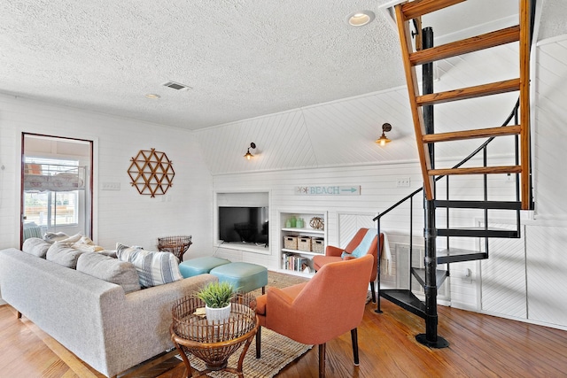 living room featuring built in shelves, wood walls, wood-type flooring, and a textured ceiling