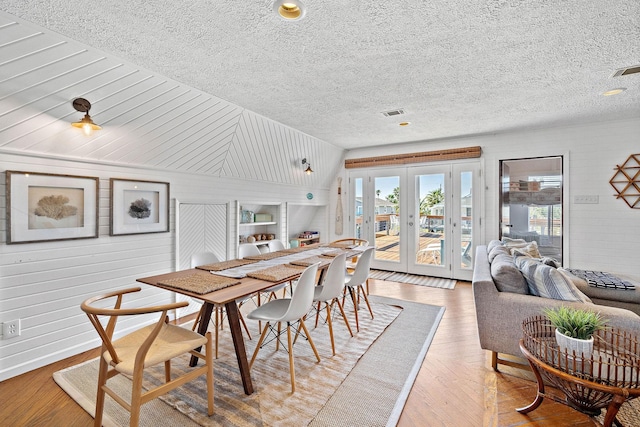 dining room featuring wooden walls, french doors, lofted ceiling, and hardwood / wood-style flooring