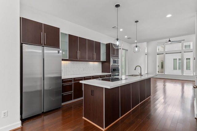 kitchen featuring decorative backsplash, ceiling fan, a kitchen island with sink, sink, and built in appliances