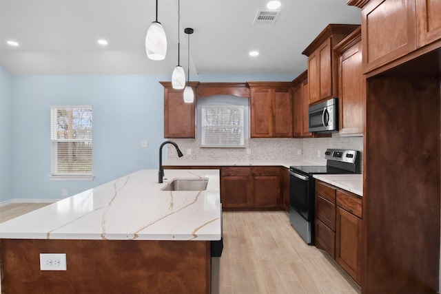 kitchen with light stone counters, stainless steel appliances, sink, light hardwood / wood-style floors, and hanging light fixtures