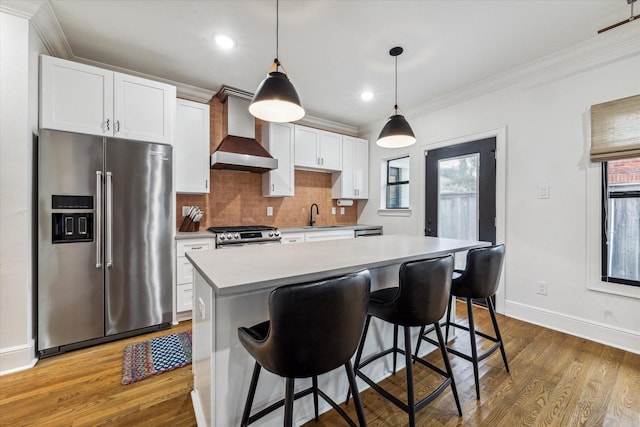 kitchen with appliances with stainless steel finishes, wall chimney exhaust hood, pendant lighting, white cabinets, and a center island