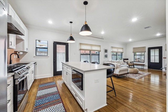 kitchen with stainless steel gas range, a breakfast bar, a kitchen island, built in microwave, and white cabinetry