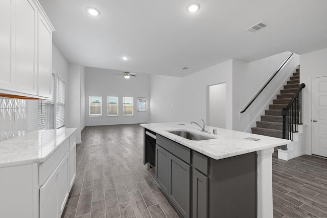 kitchen featuring dark wood-type flooring, sink, ceiling fan, an island with sink, and white cabinetry