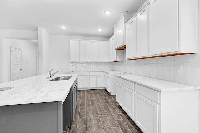 kitchen featuring sink, dark hardwood / wood-style floors, an island with sink, light stone counters, and white cabinetry