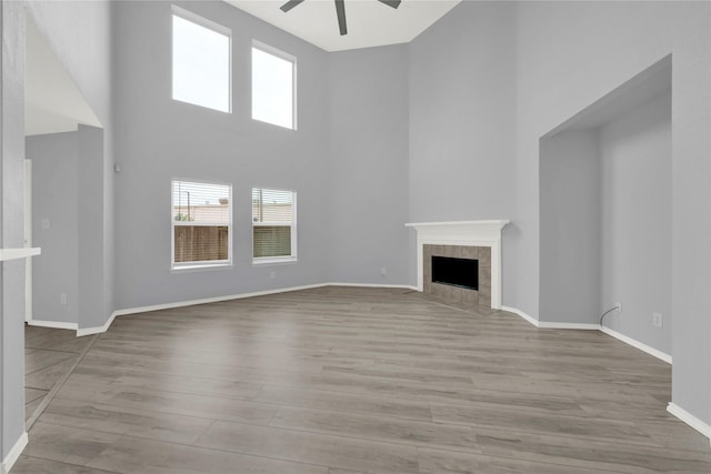 unfurnished living room with a tile fireplace, ceiling fan, light hardwood / wood-style floors, and a high ceiling