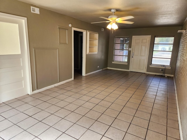 empty room featuring brick wall, ceiling fan, and light tile patterned flooring