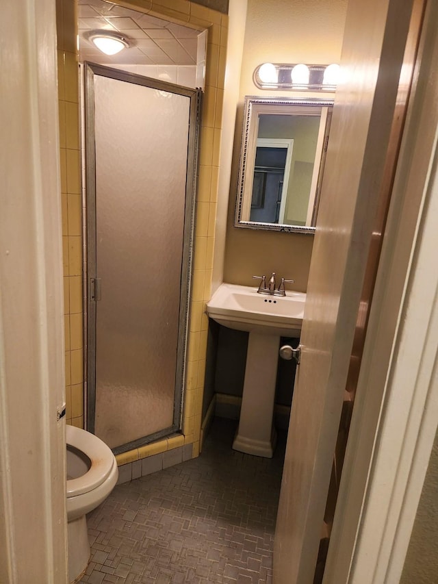 bathroom featuring sink, a shower with shower door, and toilet