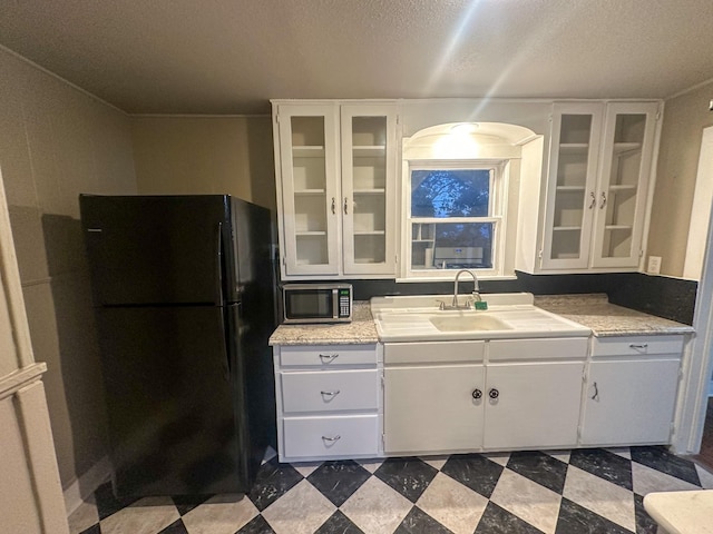 kitchen with black refrigerator, a textured ceiling, white cabinets, and sink