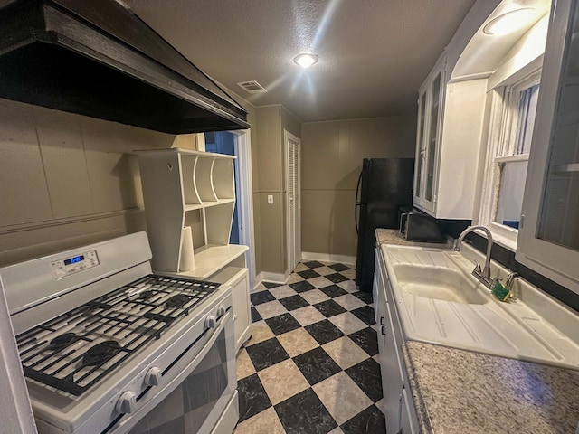 kitchen with black refrigerator, gas range, a textured ceiling, sink, and white cabinetry