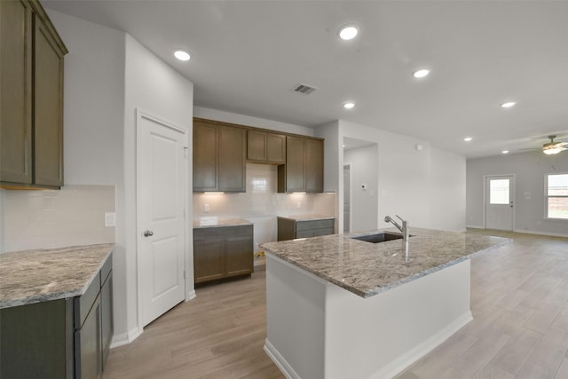 kitchen featuring tasteful backsplash, light stone counters, ceiling fan, sink, and an island with sink