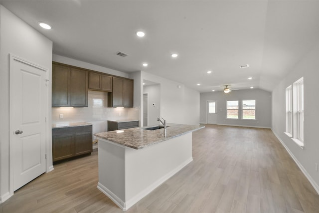 kitchen featuring sink, decorative backsplash, ceiling fan, light stone countertops, and an island with sink