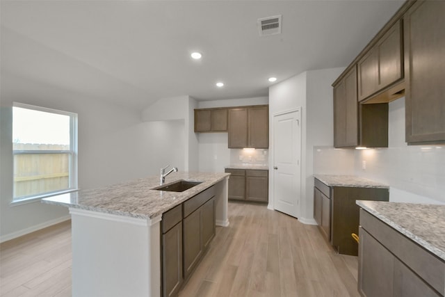 kitchen featuring decorative backsplash, sink, an island with sink, and light wood-type flooring