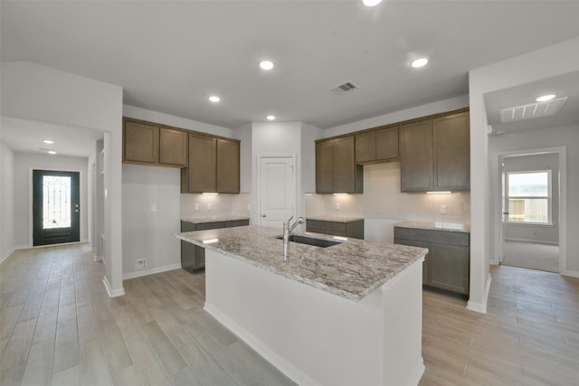 kitchen featuring a healthy amount of sunlight, light stone countertops, sink, and an island with sink