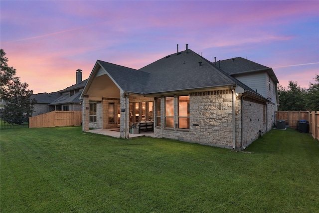 back of house at dusk with stone siding, a shingled roof, a patio area, and fence private yard