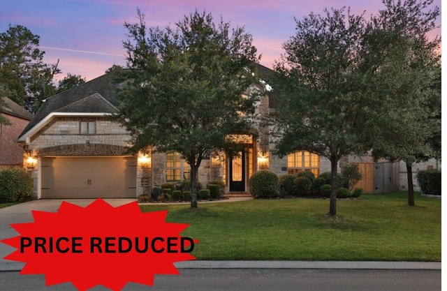 view of front of home featuring an attached garage, stone siding, driveway, and a yard