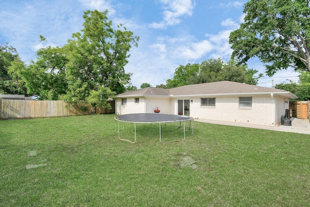 rear view of property with a yard and a trampoline