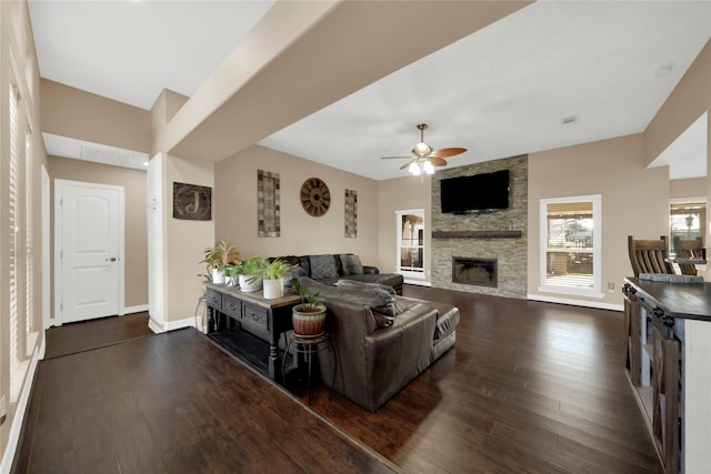 living room featuring ceiling fan, a fireplace, and dark wood-type flooring