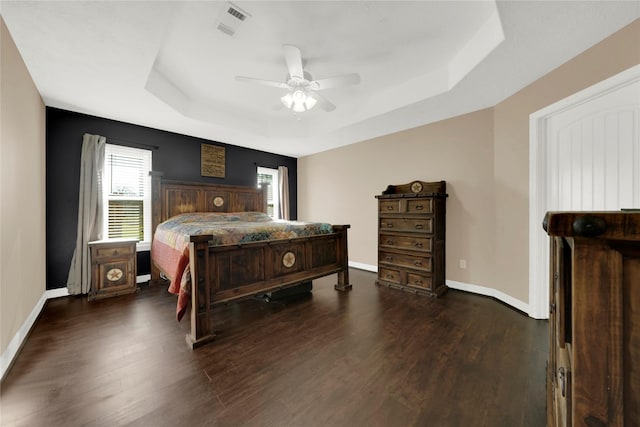 bedroom with ceiling fan, dark hardwood / wood-style floors, and a raised ceiling