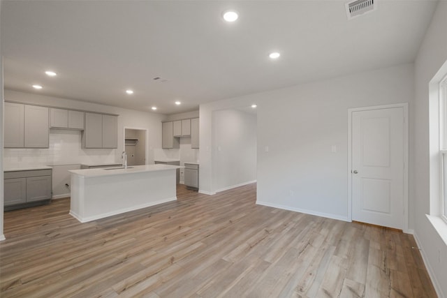 kitchen featuring backsplash, sink, gray cabinets, an island with sink, and light hardwood / wood-style floors