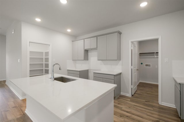 kitchen with dark hardwood / wood-style flooring, backsplash, gray cabinetry, a kitchen island with sink, and sink