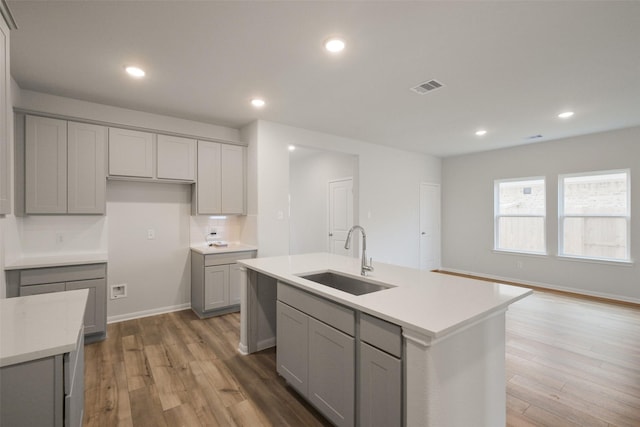 kitchen with backsplash, a center island with sink, gray cabinets, and sink