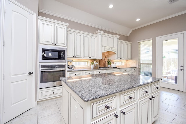 kitchen with light tile patterned floors, appliances with stainless steel finishes, tasteful backsplash, a kitchen island, and light stone counters