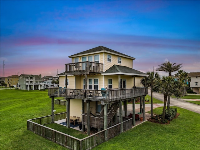 back house at dusk featuring a wooden deck, a yard, a balcony, and a patio