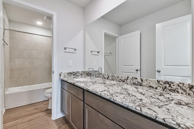 full bathroom featuring hardwood / wood-style flooring, vanity, tiled shower / bath combo, and toilet