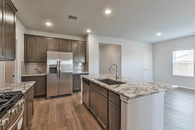 kitchen with sink, light stone countertops, an island with sink, tasteful backsplash, and stainless steel appliances