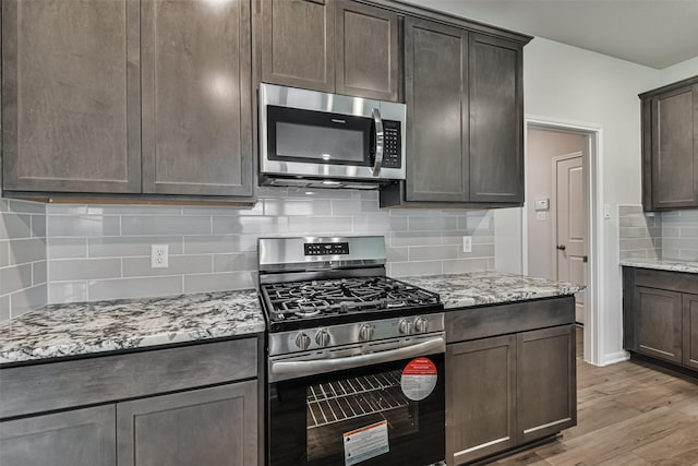 kitchen featuring decorative backsplash, appliances with stainless steel finishes, light stone counters, dark brown cabinets, and light hardwood / wood-style flooring